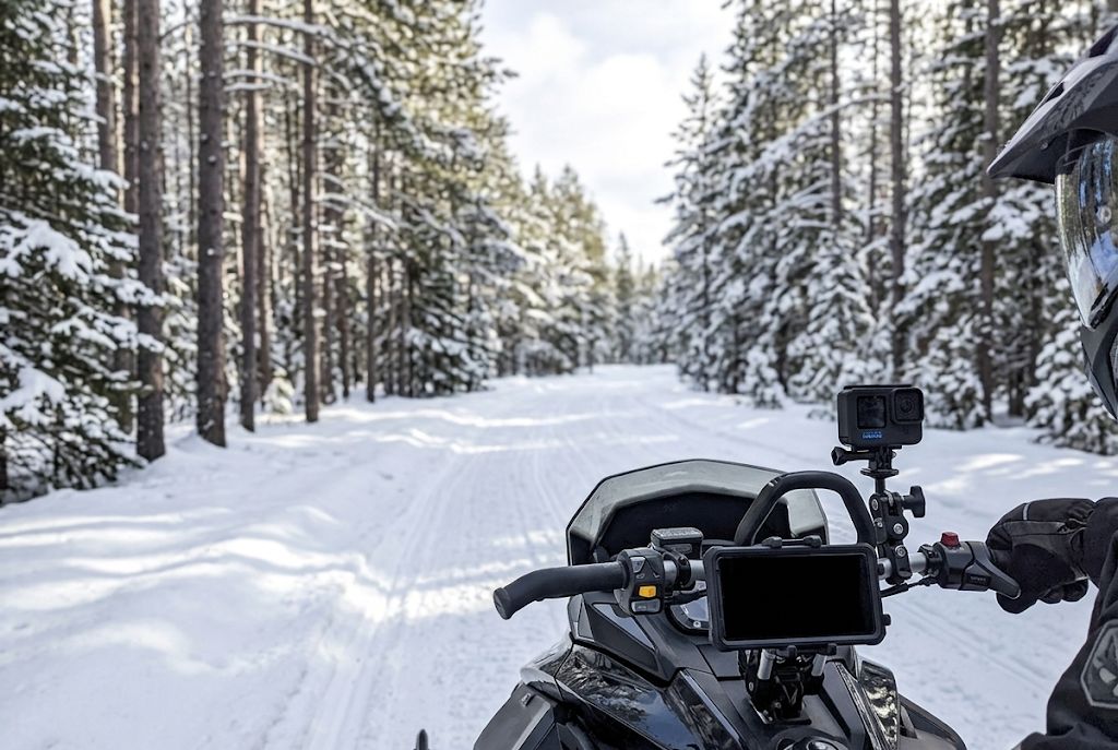 Phone mount and GoPro mount on snowmobile handlebars on snowy trail